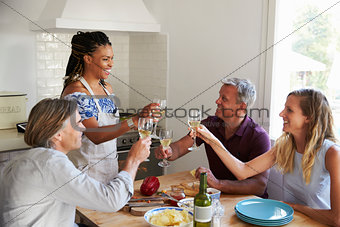 Two couples preparing dinner make a toast at kitchen table