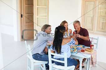 Two couples at dinner on a patio make a toast, back view