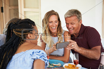 Friends at a dinner table look at pictures on a smartphone