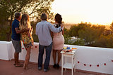 Two couples admire view from rooftop at sunset, full length