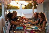 Two couples making a toast at dinner on a rooftop terrace