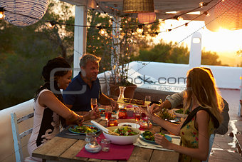 Two couples eating dinner at sunset on a rooftop terrace