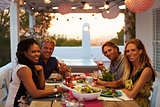 Two couples having dinner on a roof terrace look to camera
