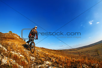 Wide angle view of a cyclist riding a bike on a nature trail in the mountains.