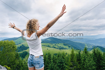 Woman standing on cliff's edge with raised hands
