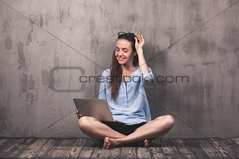 Young smiling woman sitting on the wooden floor with laptop