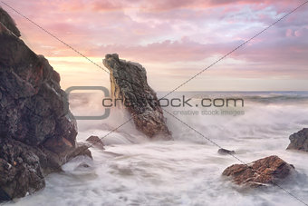 Wave surges through rocky coastline at sunrise