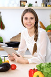 Young  happy woman is making online shopping by tablet computer while smiling. Housewife looking for a new recipe for  cooking in a kitchen