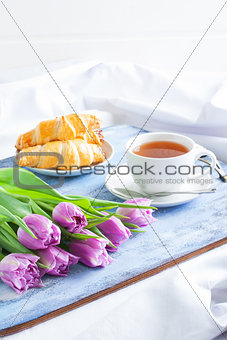 Breakfast with croissants tea purple tulips on blue wooden tray.