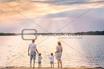 View from behind of happy family watching the sunset and sailboa