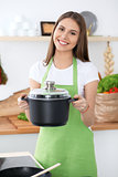 Young happy woman in a green apron cooking in the kitchen. Housewife found a new recipe for her soup. Healthy food and vegetarian concept