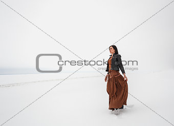 Girl in ethnic costume standing in a field, which is covered with snow