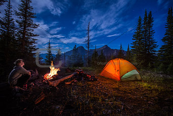 Man looking up at the stars next to campfire and tent at night