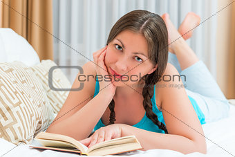 brunette girl with a book lying on the bed