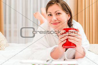 resting girl in bathrobe drinking tea in bed