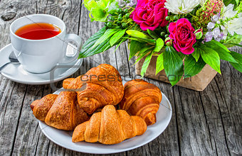 croissants, tea and flowers on an old wooden table