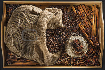 Linen bag with coffee grains, a hank of a cord, a stick of cinnamon, berry of a juniper and fruits of an anisetree on a tray from a bamboo