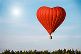 Red air balloon in the shape of a heart flying in blue sky