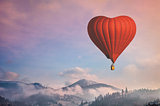 Red air balloon in the shape of a heart flying in morning mountains
