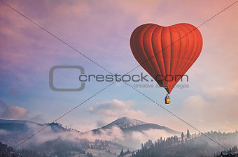 Red air balloon in the shape of a heart flying in morning mountains
