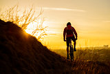 Silhouette of Enduro Cyclist Riding the Mountain Bike on the Rocky Trail at Sunset. Active Lifestyle Concept. Space for Text.