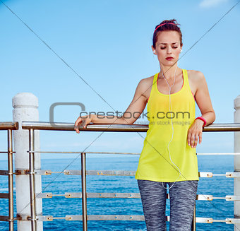 Healthy woman in fitness outfit listening to music at embankment