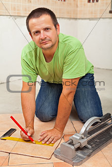 Man laying ceramic floor tiles in a new building