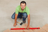 Man laying ceramic floor tiles - checking with a level, top view
