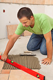 Man laying ceramic floor tiles - checking lines with a level