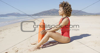 Lifeguard sitting with rescue float on beach