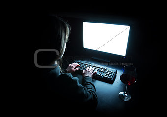 Silhouette of woman typing at computer in dark illuminated by screen