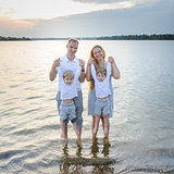 Happy family - father, mother, two sons on the beach with their feet in the water at sunset