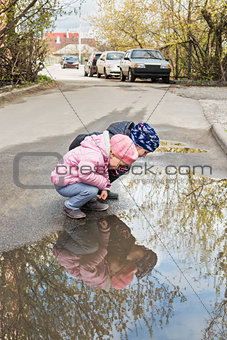 Two children look in a puddle