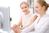 Two blonde business women sitting at the desk in office