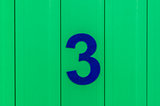 the number three, blue, set against bright green wood