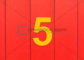 the number five, yellow, set against bright red wood