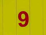 the number nine, red, set against bright yellow wood