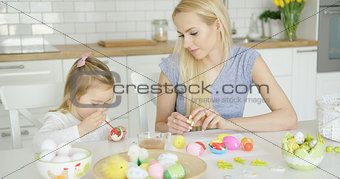 Mother looking at girl coloring eggs