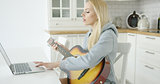 Woman using laptop while playing guitar