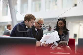 Businesspeople Discuss Document In Lobby Of Modern Office