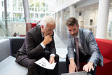 Two Businessmen Meeting In Lobby Area Of Modern Office