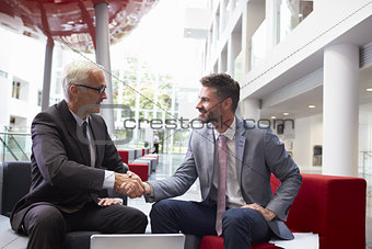 Two Businessmen Shaking Hands In Lobby Of Modern Office