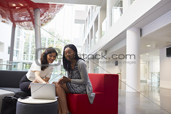 Two Businesswomen Using Laptop In Lobby Of Modern Office