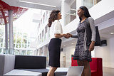 Two Businesswomen Shaking Hands In Lobby Of Modern Office
