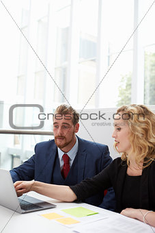 Two Businesspeople Using Laptop At Desk In Modern Office