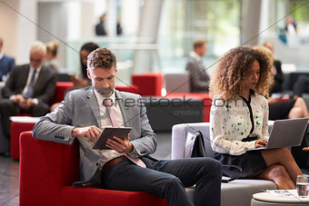 Businesspeople Using Digital Devices In Busy Office Lobby
