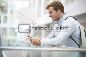 Adult male student using smartphone in university interior