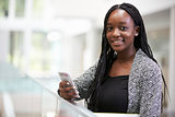 Young black female student holding phone in university foyer