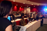 Woman lecturing students in lecture theatre, focus foreground