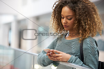 Smiling mixed race young woman uses phone in modern interior